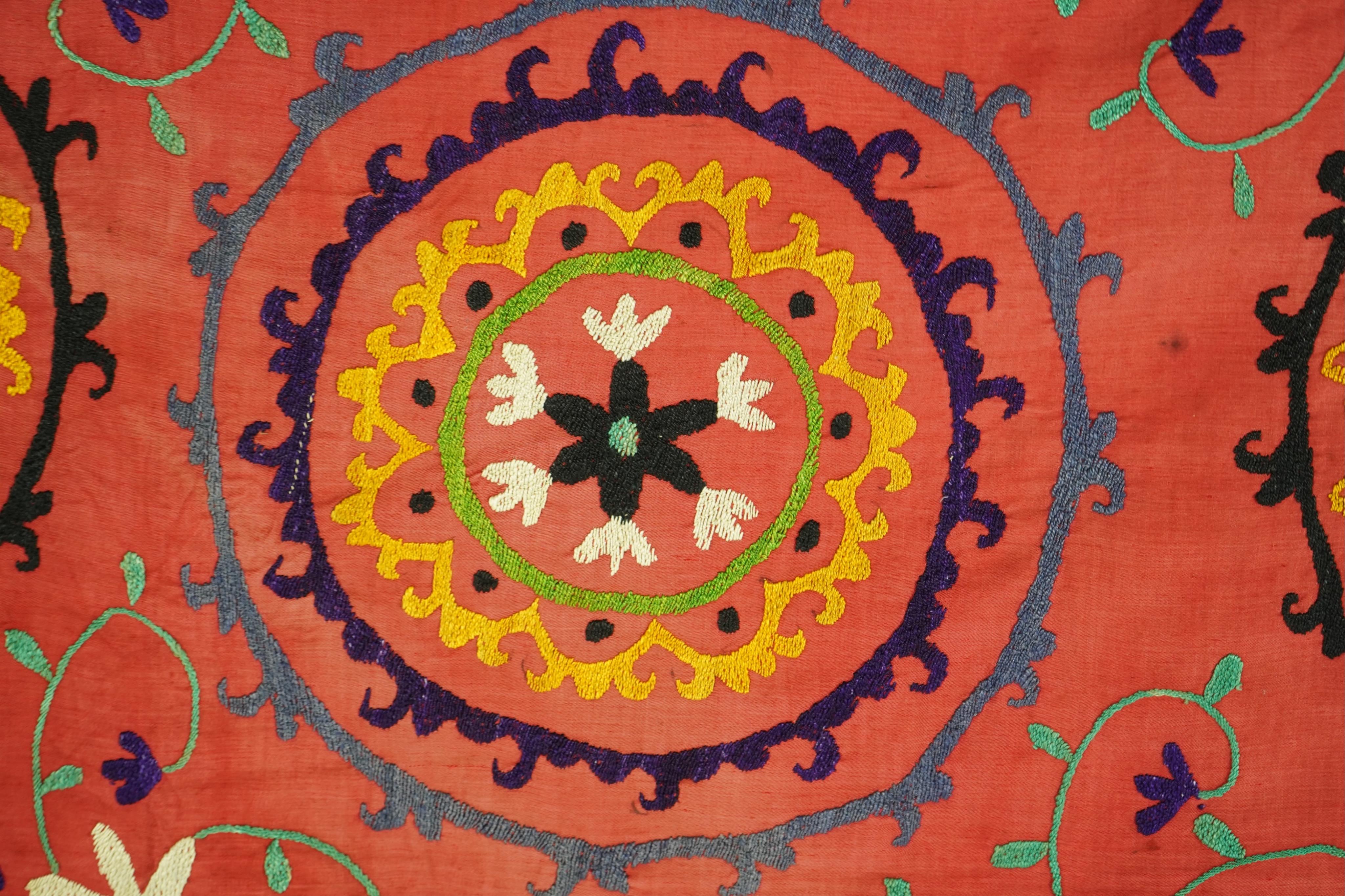 A large 20th century Uzbek multi coloured and embroidered Suzani wall hanging. The word Suzani meaning needlepoint in Farsi. Made in three panels embroidered on a rich dark red background, using large stylised multi colo